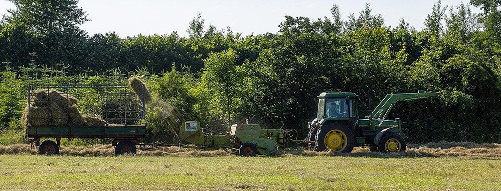 Traktor mit Ballenpresse und Ladewagen bei der Heuernte